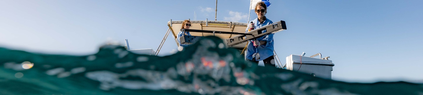 Scientists in boat placing measuring equipment into sea